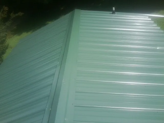 New green metal panels meeting at the ridge of a roof — Flat Roof Repair work by our crew in North Bend