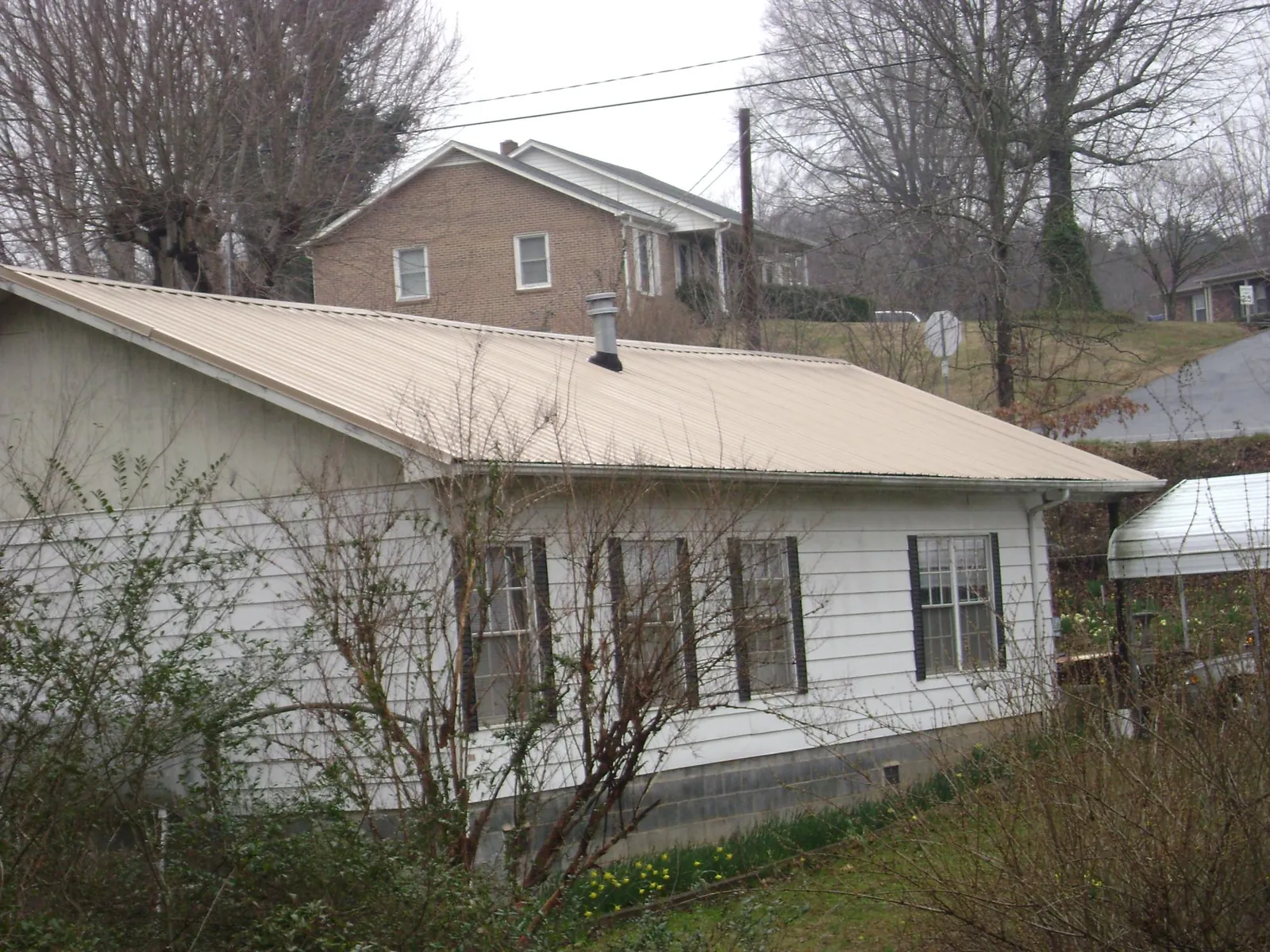 Tan metal roof on a white sided house set into a hillside — Commercial Roofing by Roofing Brothers in North Bend
